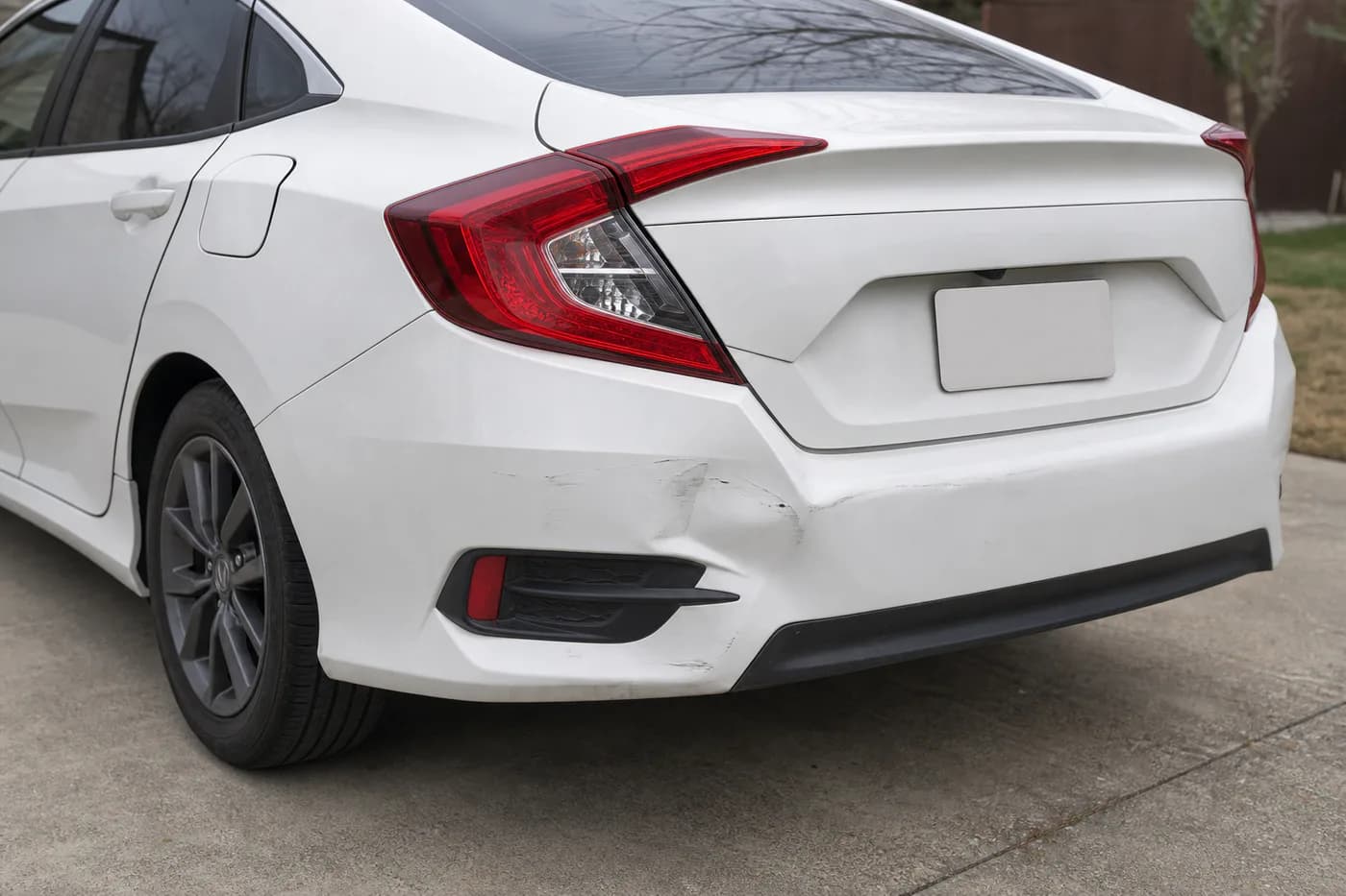 White compact sedan with a moderate rear bumper dent and paint scuffing
